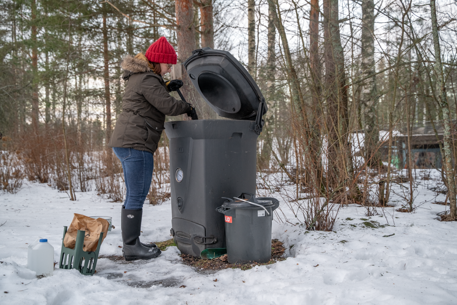 Nainen hoitamassa kompostoria talvisella pihalla.