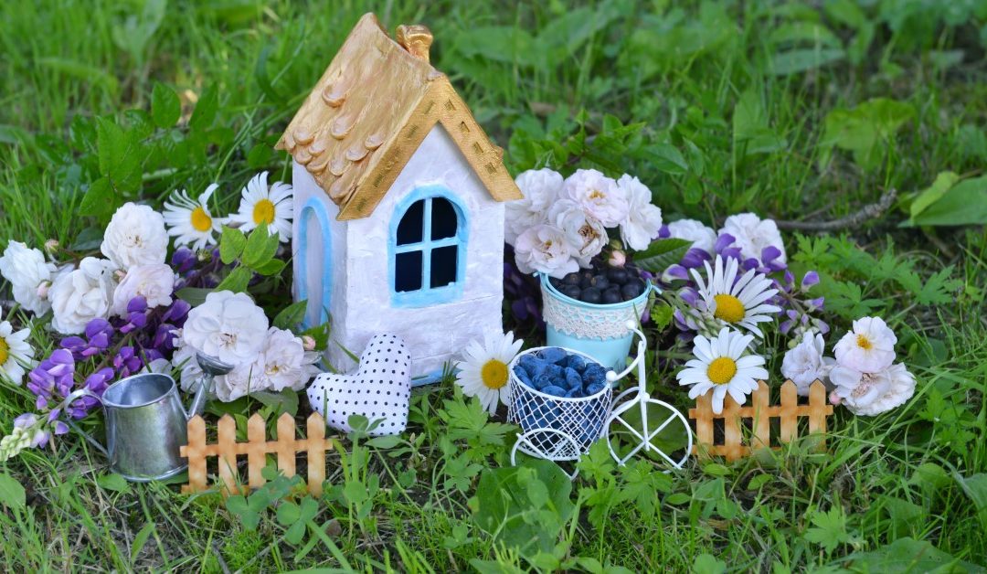 Kuvituskuva, jossa minikokoinen talo nurmikolla keskellä kukkia